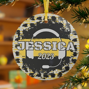 Könnte beinhalten: Runder schwarzer und gelber Weihnachtsbaumschmuck mit einem weißen Headset und dem Namen Jessica und dem Jahr 2023.