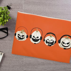 May include: Orange zippered pouch with four white pumpkins wearing black headphones. Each pumpkin has a different facial expression.