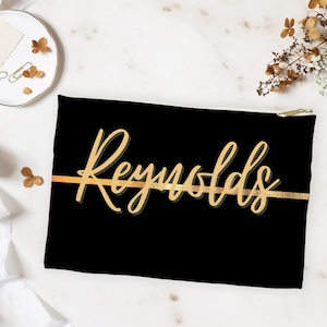May include: Black zippered pouch with a gold stripe and the name "Reynolds" written in gold script.