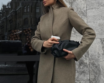 May include: A woman wearing a brown coat, black sunglasses, and a black handbag holds a to-go coffee cup.