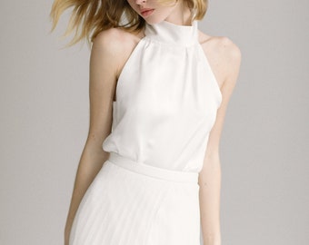 May include: A woman wearing a white halter top and a white pleated skirt. Her hair is blonde and she has blue eyeshadow.