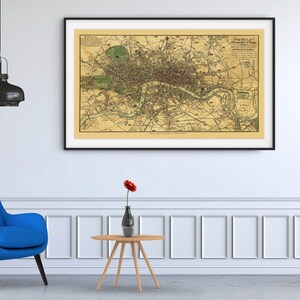 Peut inclure: Une carte vintage de Londres, en Angleterre, encadr&eacute;e en noir, est accroch&eacute;e &agrave; un mur blanc au-dessus d'un fauteuil bleu et d'une petite table en bois avec un vase de fleurs rouges. Une plante en pot est plac&eacute;e sur un support en m&eacute;tal noir &agrave; droite.
