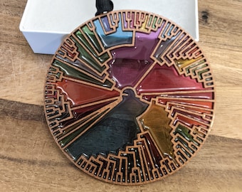 May include: A circular, copper-colored ornament with a tree-like design. The ornament is filled with colorful, translucent resin, creating a stained glass effect. The design is reminiscent of a phylogenetic tree, representing the evolutionary relationships between different species.