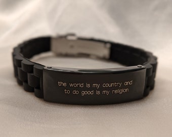 May include: Black silicone bracelet with a silver clasp and a black metal plate engraved with the quote "the world is my country and to do good is my religion".