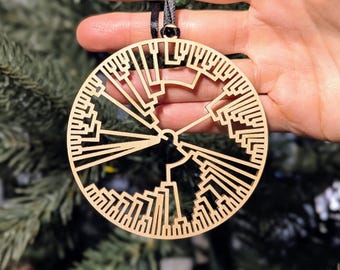 May include: A round, wooden Christmas ornament with a complex, geometric design. The ornament is light brown and has a black ribbon for hanging. The design is a series of interconnected lines and shapes.