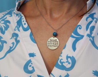 May include: A silver necklace with a round pendant that reads "the world is my country and to do good is my religion". The pendant is attached to a silver chain and has a blue gemstone bead.