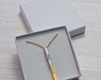May include: A gold necklace with a silver bar pendant. The bar is engraved with the words "Imagine" and "No Religion". The necklace is displayed in a white box with a white background.