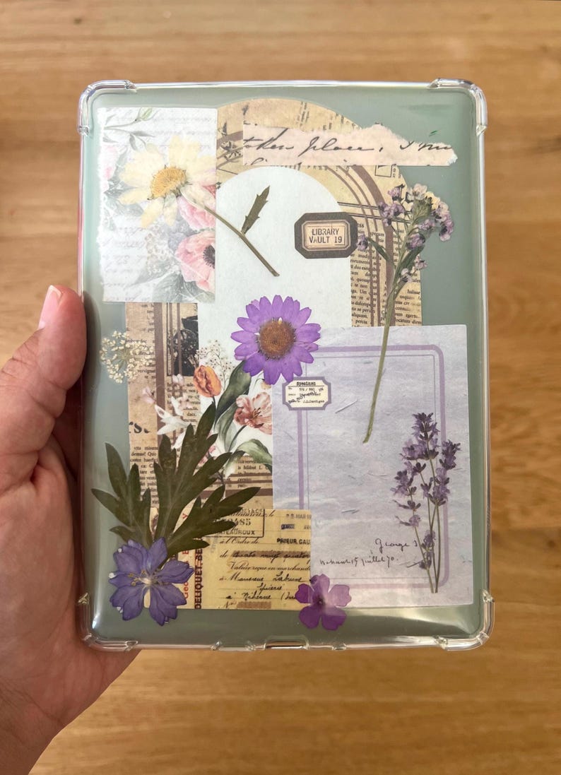 May include: Clear phone case with a collage of dried flowers, vintage paper, and the text "LIBRARY VAULT 19." The design includes purple, pink, and yellow flowers, with green leaves and a light green background.