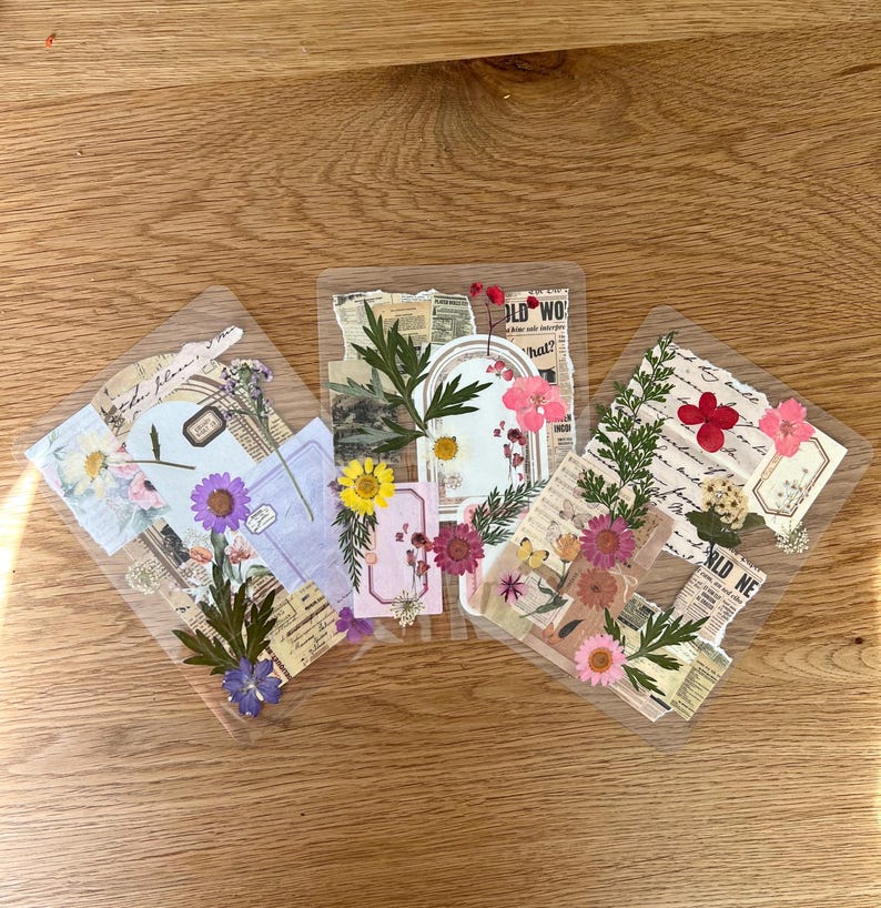 May include: Three clear, rectangular stickers with pressed flowers, paper ephemera, and text. The stickers feature various colors of flowers, including pink, yellow, and purple. The text includes the words "OLD WO" and "hat?"