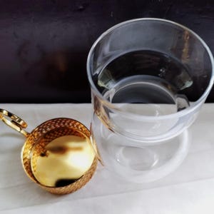 Puede incluir: Una taza de t&eacute; de cristal transparente con un borde ancho y un colador de t&eacute; de metal dorado independiente. El colador presenta un cuerpo de malla fina, una base s&oacute;lida de tono dorado y un peque&ntilde;o asa circular en el lateral para extraerlo.
