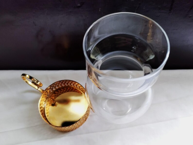 Puede incluir: Una taza de t&eacute; de cristal transparente con un borde ancho y un colador de t&eacute; de metal dorado independiente. El colador presenta un cuerpo de malla fina, una base s&oacute;lida de tono dorado y un peque&ntilde;o asa circular en el lateral para extraerlo.
