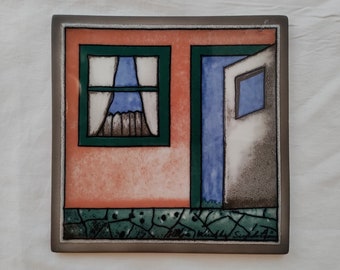 May include: A ceramic tile with a painted image of a house with a window and a door. The house is painted in shades of orange, green, blue, and gray.