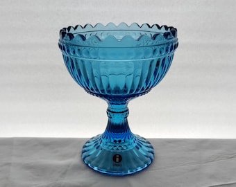 Op de afbeelding: Een grote, blauwe glazen kom met een voet. De kom heeft een gegolfde rand en een getextureerd ontwerp. De voet is gemarkeerd met het woord "Iittala".