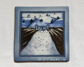 May include: A square ceramic tile featuring a hand-painted landscape scene of a snow-covered path leading to a gate, flanked by dark brown fields and blue hills. The bottom edge displays the handwritten signature H. L-S Italia-80 in white paint.