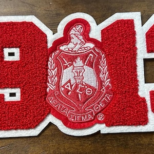 May include: A red and white patch with the number "1913" in a varsity-style font. The number is filled with a textured material. The center features a crest with text and a figure.