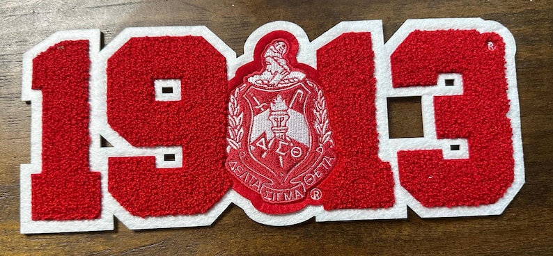 May include: A red and white patch with the number "1913" in a varsity-style font. The number is filled with a textured material. The center features a crest with text and a figure.