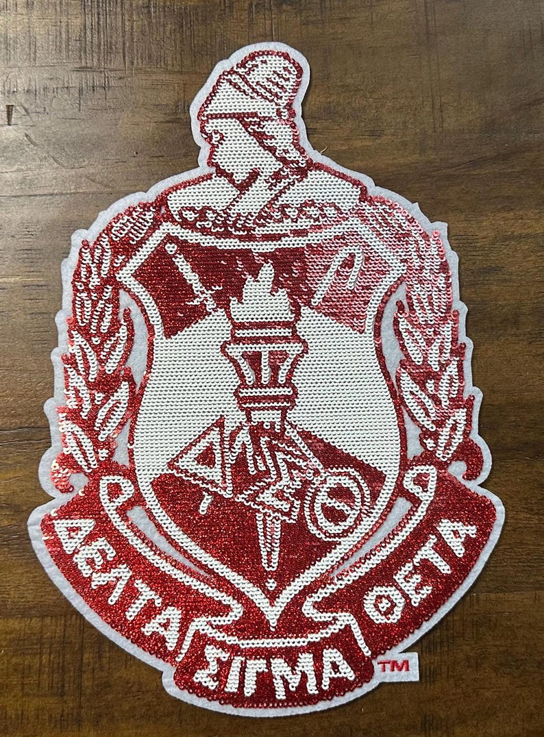 May include: Red and white sequined patch featuring the Greek letters Delta, Sigma, and Theta, with a torch and a figure in a helmet. The patch has a shield shape with a white border and the text "Delta Sigma Theta".