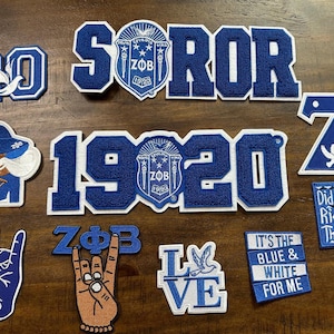 May include: A selection of blue and white embroidered patches. Features the word "SOROR", the number "20", the year "1920", the letter "Z", and the words "LOVE" and "IT'S THE BLUE & WHITE FOR ME".