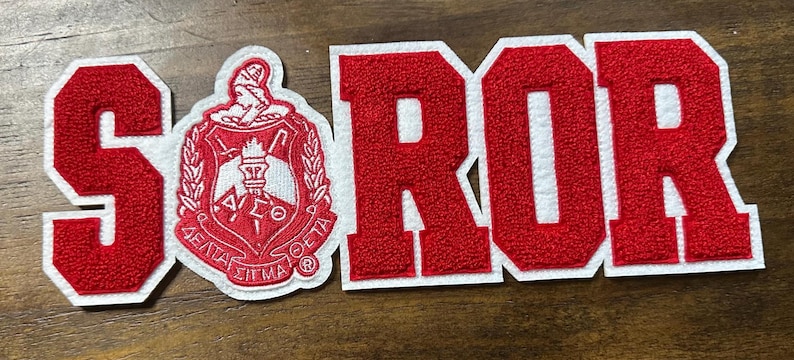 May include: Red and white embroidered patches spelling out "SOROR" with a Greek sorority crest. The letters are red with a white border. The crest is red and white with Greek letters.