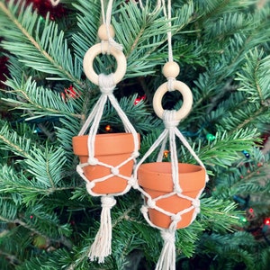 May include: Two terracotta pots with macrame hangers and wooden rings, hanging from a Christmas tree.