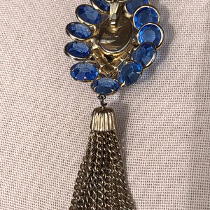 May include: A gold chain necklace with a blue rhinestone pendant and a gold tassel.
