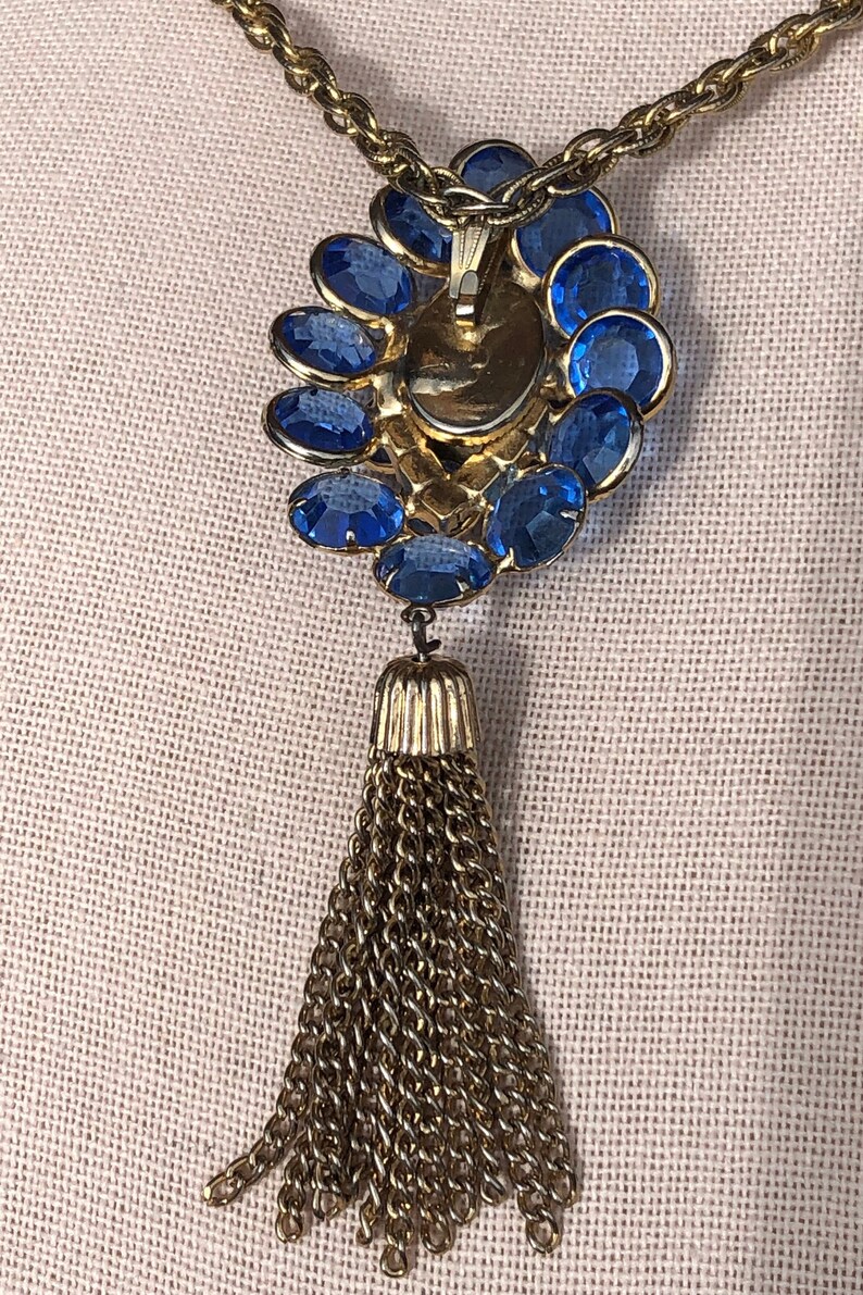 May include: A gold chain necklace with a blue rhinestone pendant and a gold tassel.