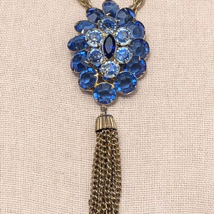 May include: A gold chain necklace with a blue rhinestone pendant and a gold tassel.