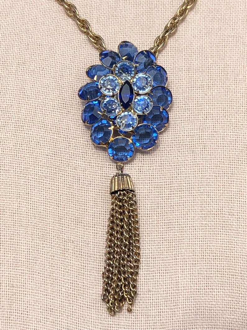 May include: A gold chain necklace with a blue rhinestone pendant and a gold tassel.