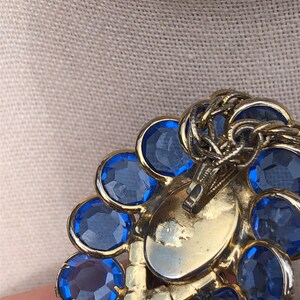 May include: Gold tone brooch with a cluster of blue rhinestones. The brooch has a hinged clasp on the back.