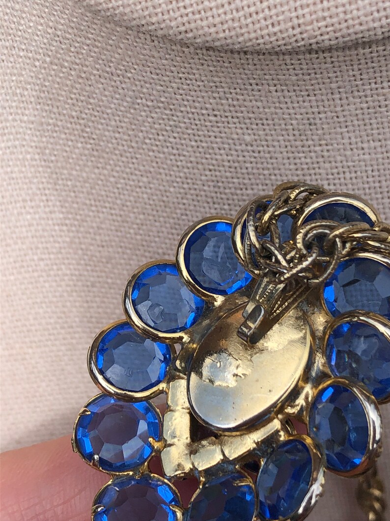 May include: Gold tone brooch with a cluster of blue rhinestones. The brooch has a hinged clasp on the back.