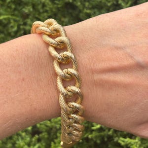 May include: A gold-toned chain link bracelet featuring a textured, dimpled surface on each individual link. The bracelet consists of a series of interlocking, rounded metal links that form a continuous, heavy-looking chain design.