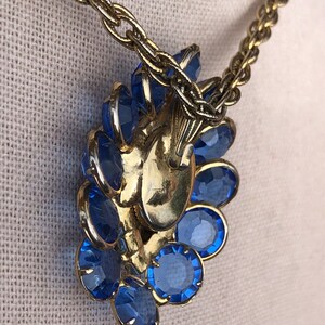 May include: A gold chain necklace with a large blue rhinestone pendant. The pendant is shaped like a flower and has a dangling drop.