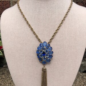 May include: A gold chain necklace with a blue rhinestone pendant and a gold tassel.