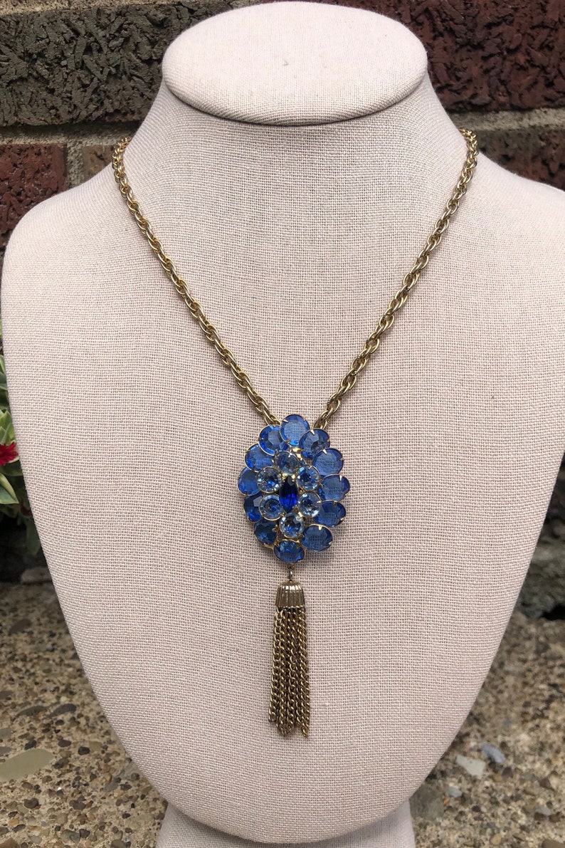 May include: A gold chain necklace with a blue rhinestone pendant and a gold tassel.
