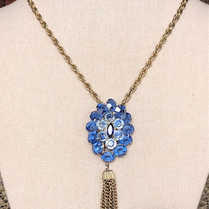 May include: A gold chain necklace with a blue and white crystal pendant and a gold tassel.