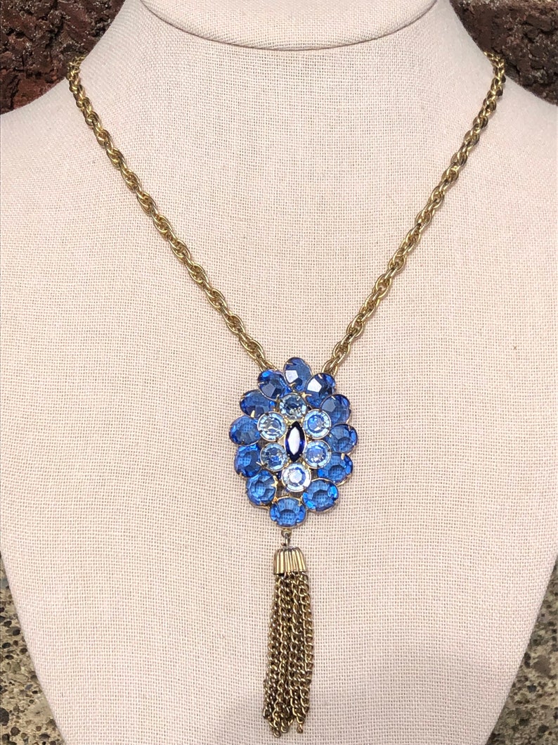 May include: A gold chain necklace with a blue and white crystal pendant and a gold tassel.