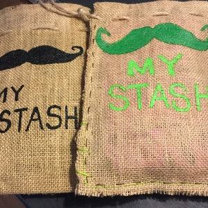 May include: Two burlap bags with black and green painted mustaches and the text "MY STASH" on each bag.