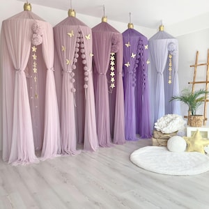 May include: Five tulle canopy beds in shades of pink and purple with gold star and butterfly decorations. The canopies are arranged in a row on a light wood floor.