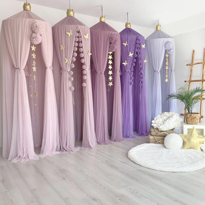 May include: Five tulle canopy beds in shades of pink and purple with gold star and butterfly decorations. The canopies are arranged in a row on a light wood floor.