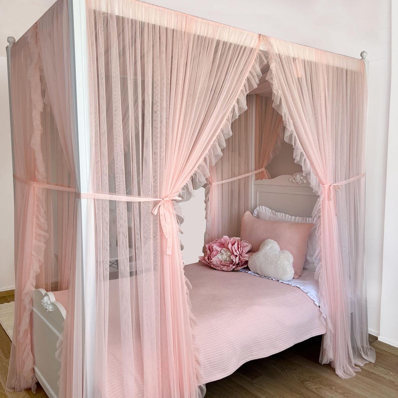 May include: A white canopy bed with a pink tulle canopy and a pink bedspread. The bed has a white headboard and footboard and is decorated with a pink flower and a white heart-shaped pillow.