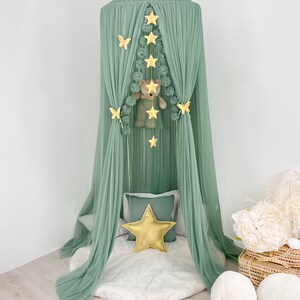 Puede incluir: Una carpa de tul verde con una corona dorada en la parte superior. La carpa est&aacute; decorada con estrellas doradas, mariposas y pompones. Un oso de peluche est&aacute; colgado dentro de la carpa.