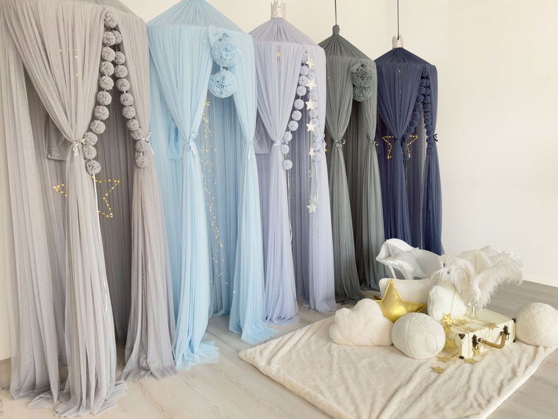 May include: A set of six sheer fabric canopy curtains with pom-pom trim and star accents. The curtains are in various shades of blue and gray.