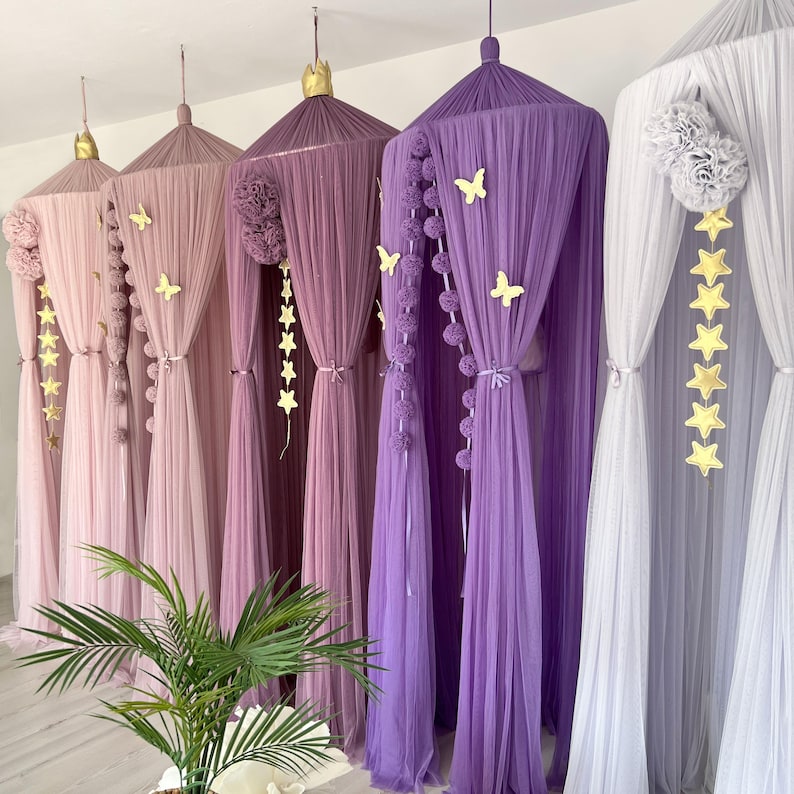 May include: Five different colored tulle canopy beds with pom poms and star decorations. The canopies are in shades of purple, pink, and white.