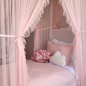 May include: A pink canopy bed with a white cloud-shaped pillow and a pink flower pillow. The bed is covered in a pink striped bedspread.