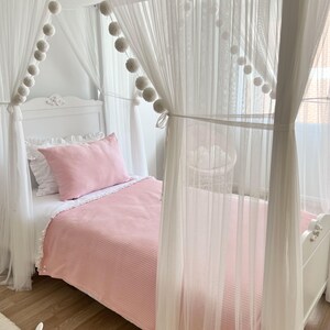 May include: A white canopy bed with a pink striped blanket and white pom poms along the canopy.