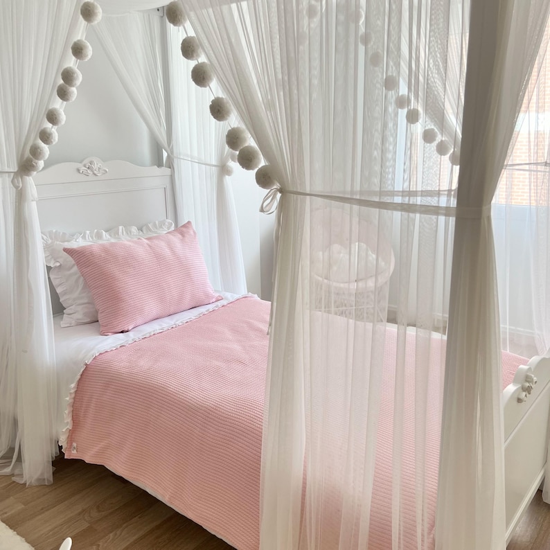 May include: A white canopy bed with a pink striped blanket and white pom poms along the canopy.