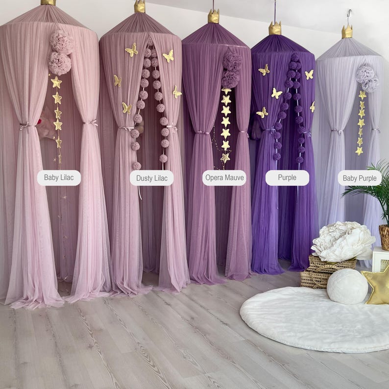 May include: Five different colored tulle canopy beds with gold star and butterfly decorations. The canopies are in shades of purple, lilac, and white. The canopies are hanging from the ceiling and are arranged in a row. The canopies are all the same size and shape. The canopies are all made of tulle and have a soft, flowing texture.