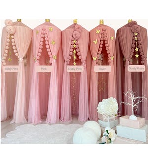 Può includere: Cinque letti a baldacchino in tulle rosa e rosa polveroso con pompon e decorazioni a forma di stella. I baldacchini sono etichettati "Baby Pink", "Pink", "Dusty Pink", "Blush" e "Dusty Rose".