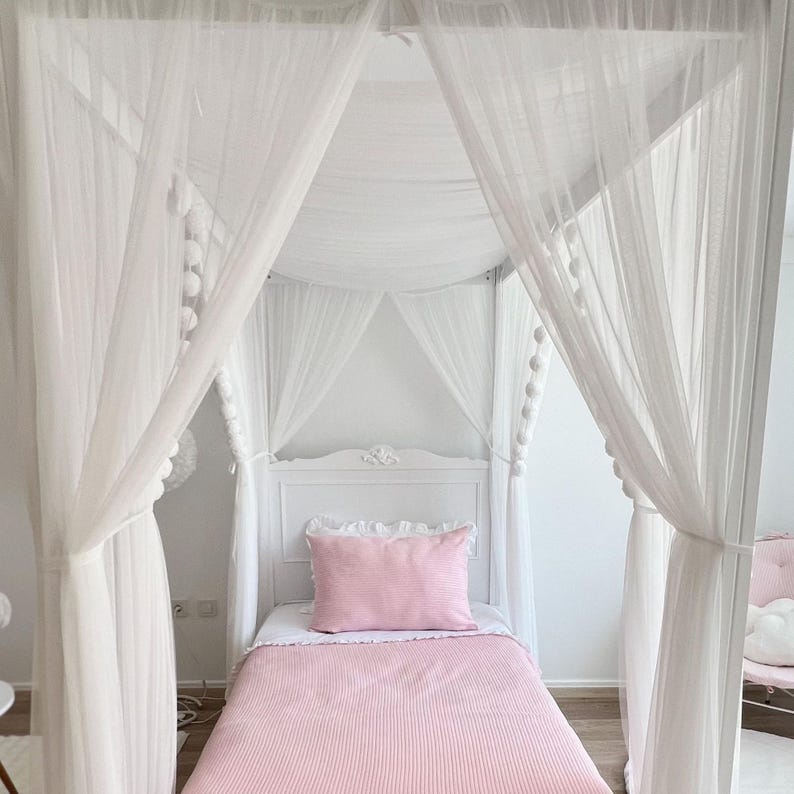 May include: A white canopy bed with a pink striped bedspread and a white sheer canopy. The canopy is decorated with white pom-poms.