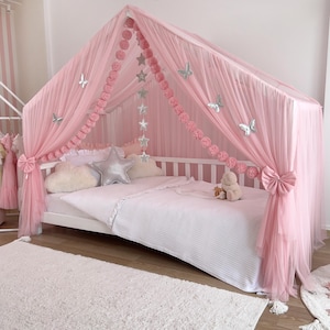 May include: A pink canopy bed with sheer draping, adorned with silver star and butterfly accents. The bed features a white frame, a white and pink striped comforter, and decorative pillows. A fluffy white rug is in the foreground.